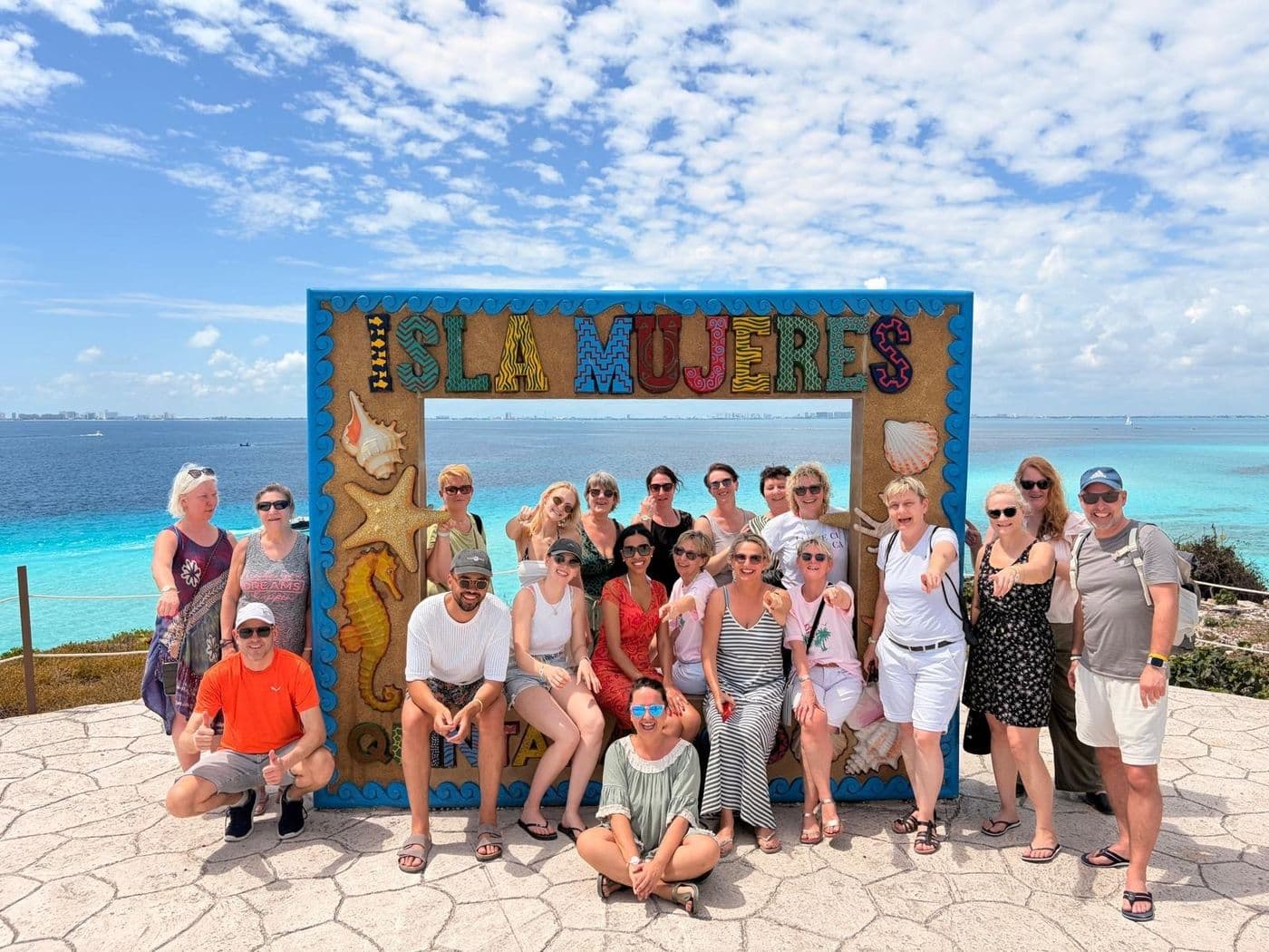 Teilnehmerinnen und Teilnehmer der Holiday-Land-Reise nach Mexiko posieren auf Isla Mujeres vor einem dekorativen Schriftzug mit Meerblick.